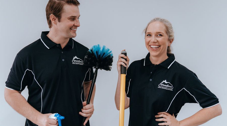 Two smiling Urban Clean staff members pose with cleaning tools in a studio portrait.