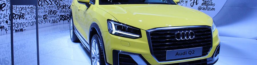 A yellow car on display in a bright showroom with a polished white floor and a digital display stand.