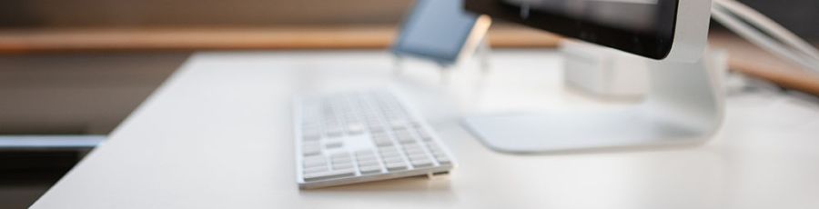 A clean, empty office desk with a monitor, keyboard and mouse beside a window looking out over a city skyline.